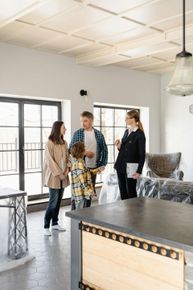 Three people talking in a bright, modern kitchen with a large island and covered furniture.