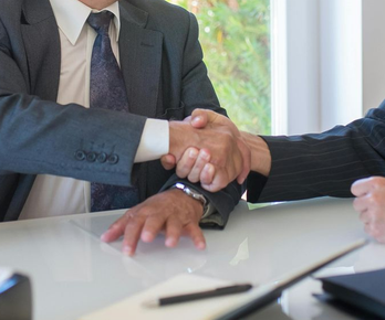 Two businesspeople in suits shaking hands across a conference table