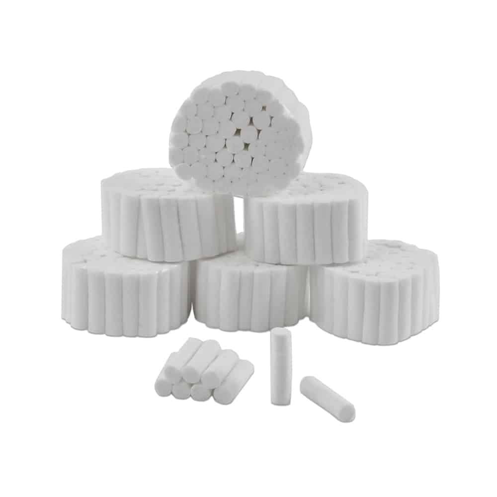 Apósitos cilíndricos blancos para heridas y rollos de gasa apilados sobre un fondo blanco.