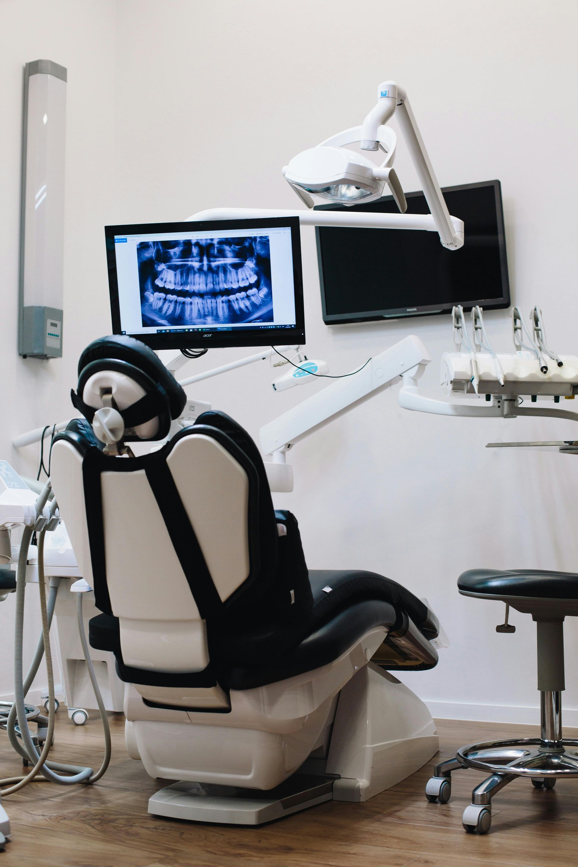Consultorio dental con un sillón de paciente vacío, un monitor y una lámpara de examen en el techo.