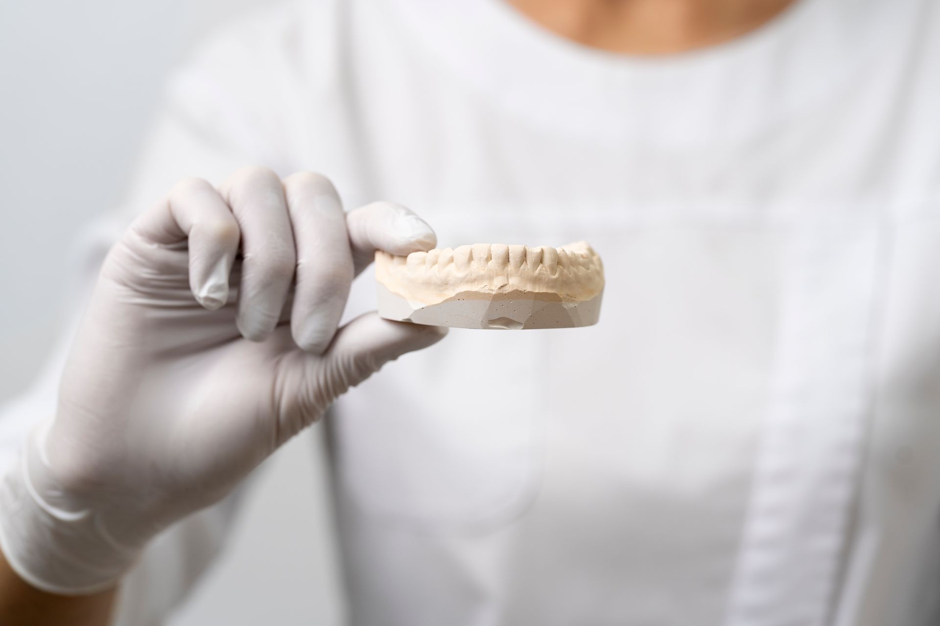 Una mano enguantada sostiene un molde dental de yeso de los dientes superiores contra una bata blanca.