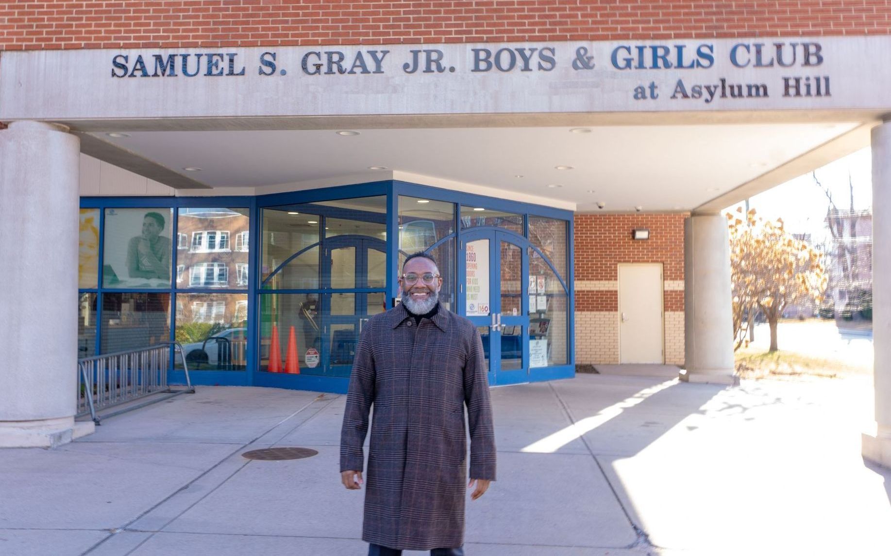 A man is standing in front of a building that says samuel s. gray jr. boys & girls club at Asylum Hill