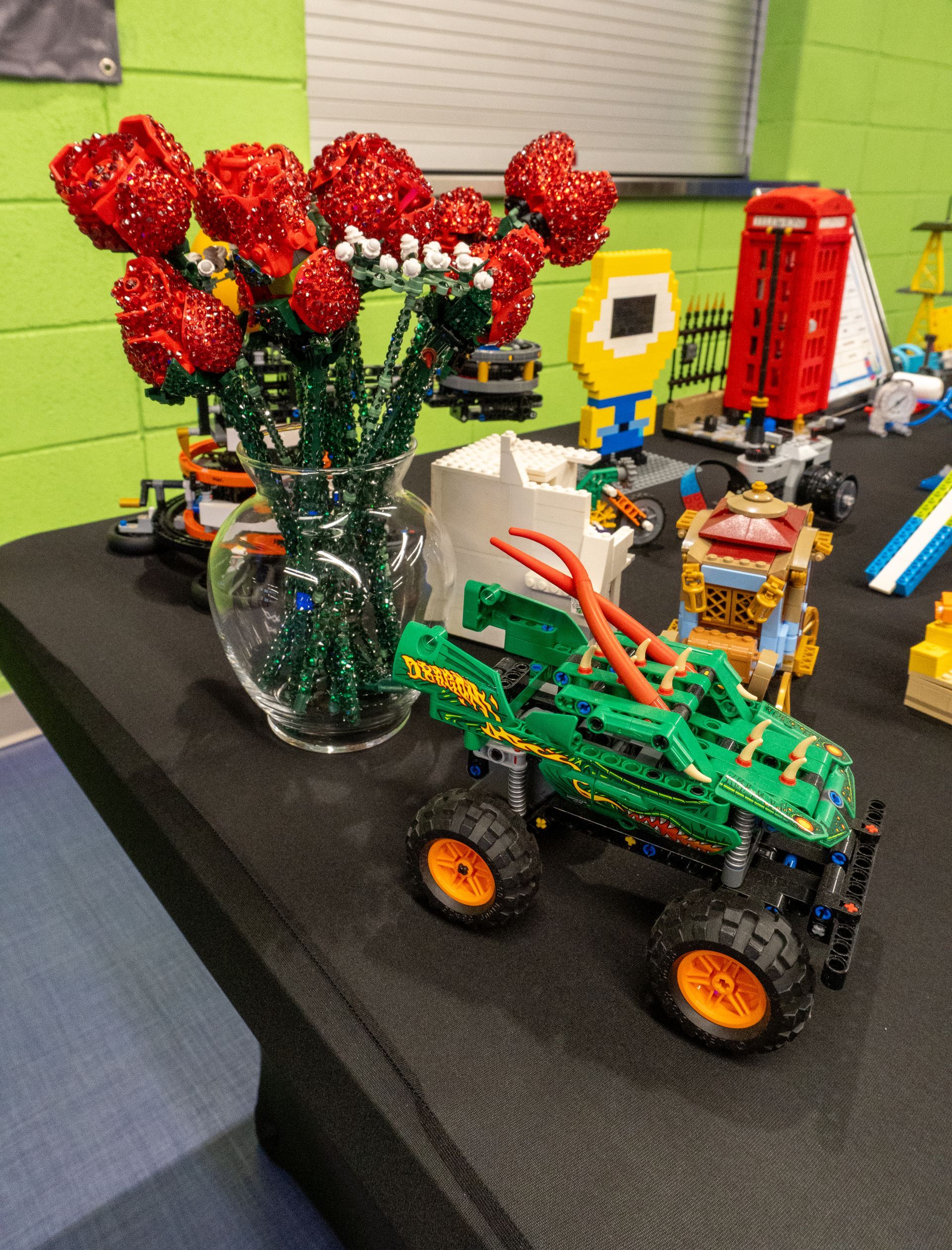 A vase of lego red roses sits on a table next to a green toy truck.