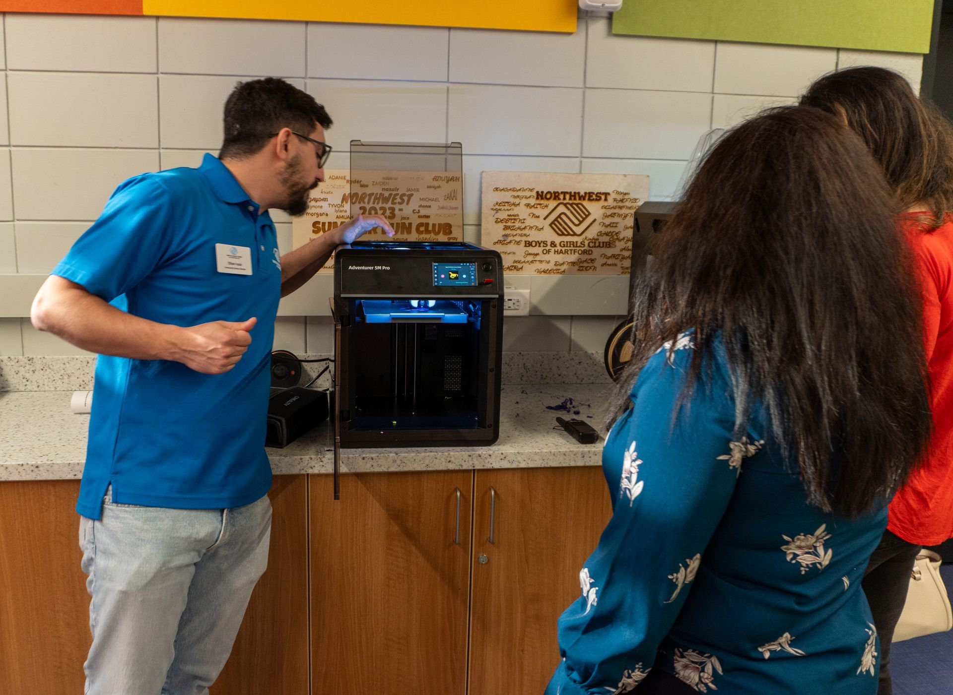 A man in a blue shirt is standing in front of a 3d printer