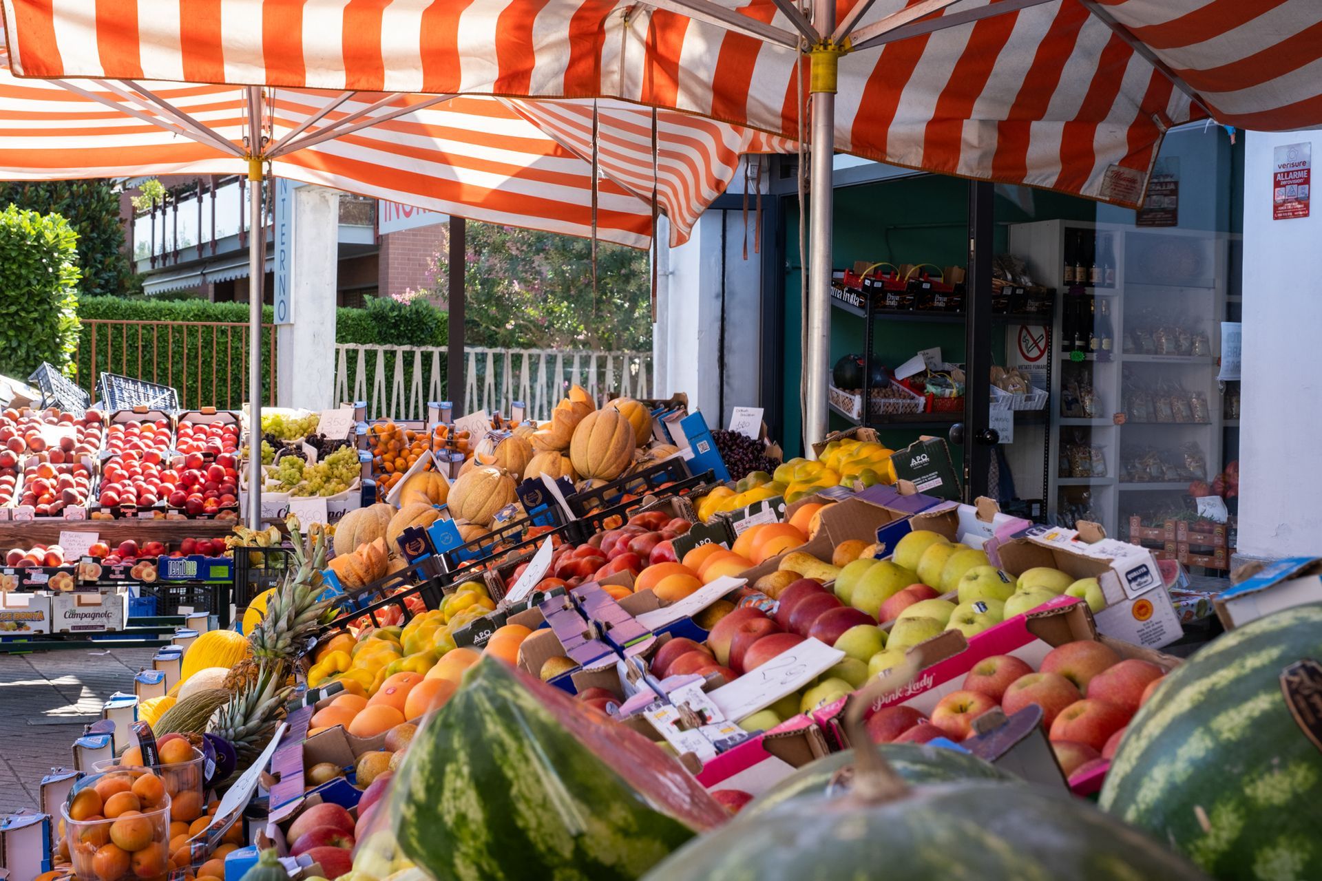 Bancarella di frutta con pile di prodotti colorati sotto una tenda a strisce arancioni e bianche