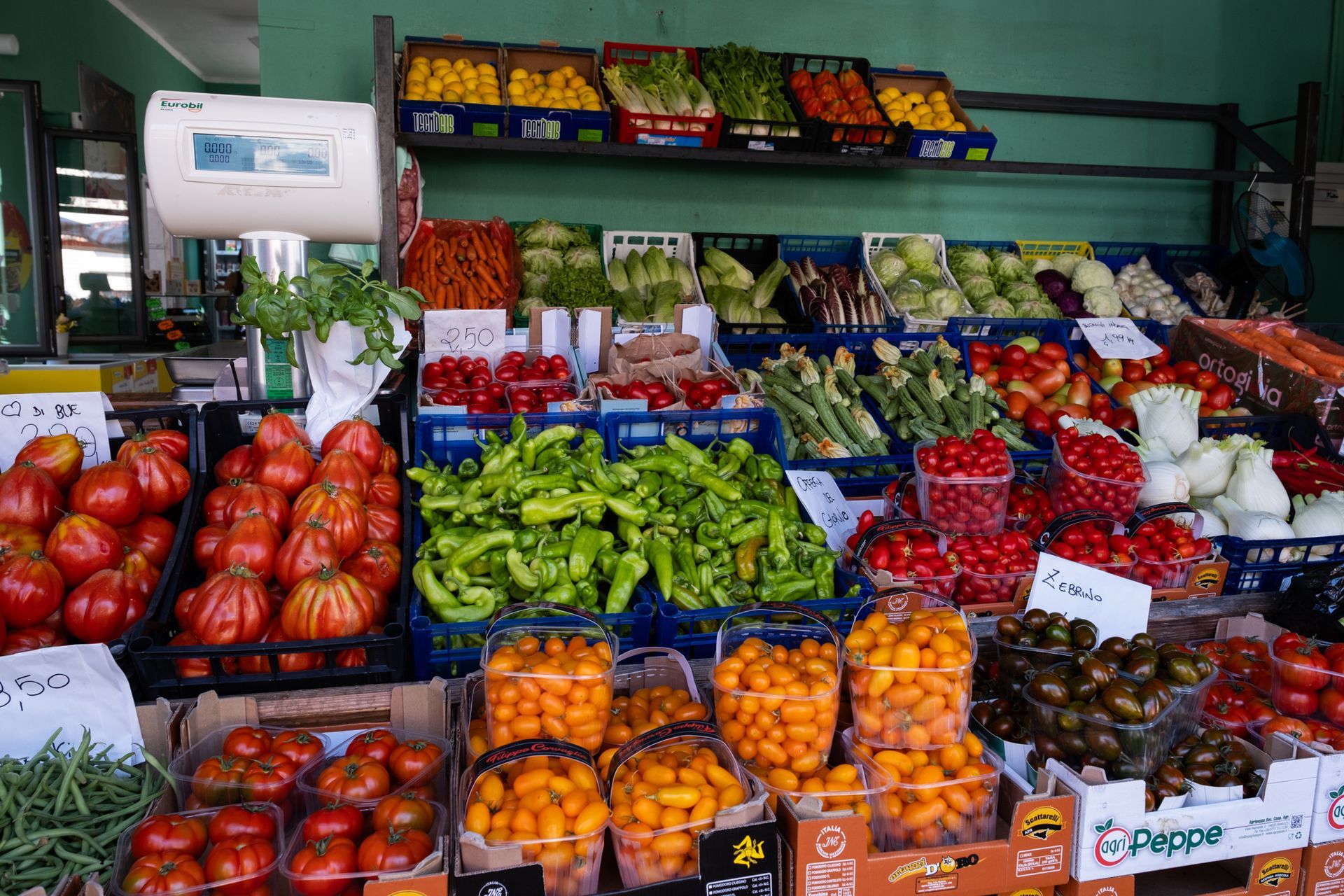 Esposizione di prodotti ortofrutticoli in un supermercato, con frutta e verdura colorata impilate in casse e scaffali.