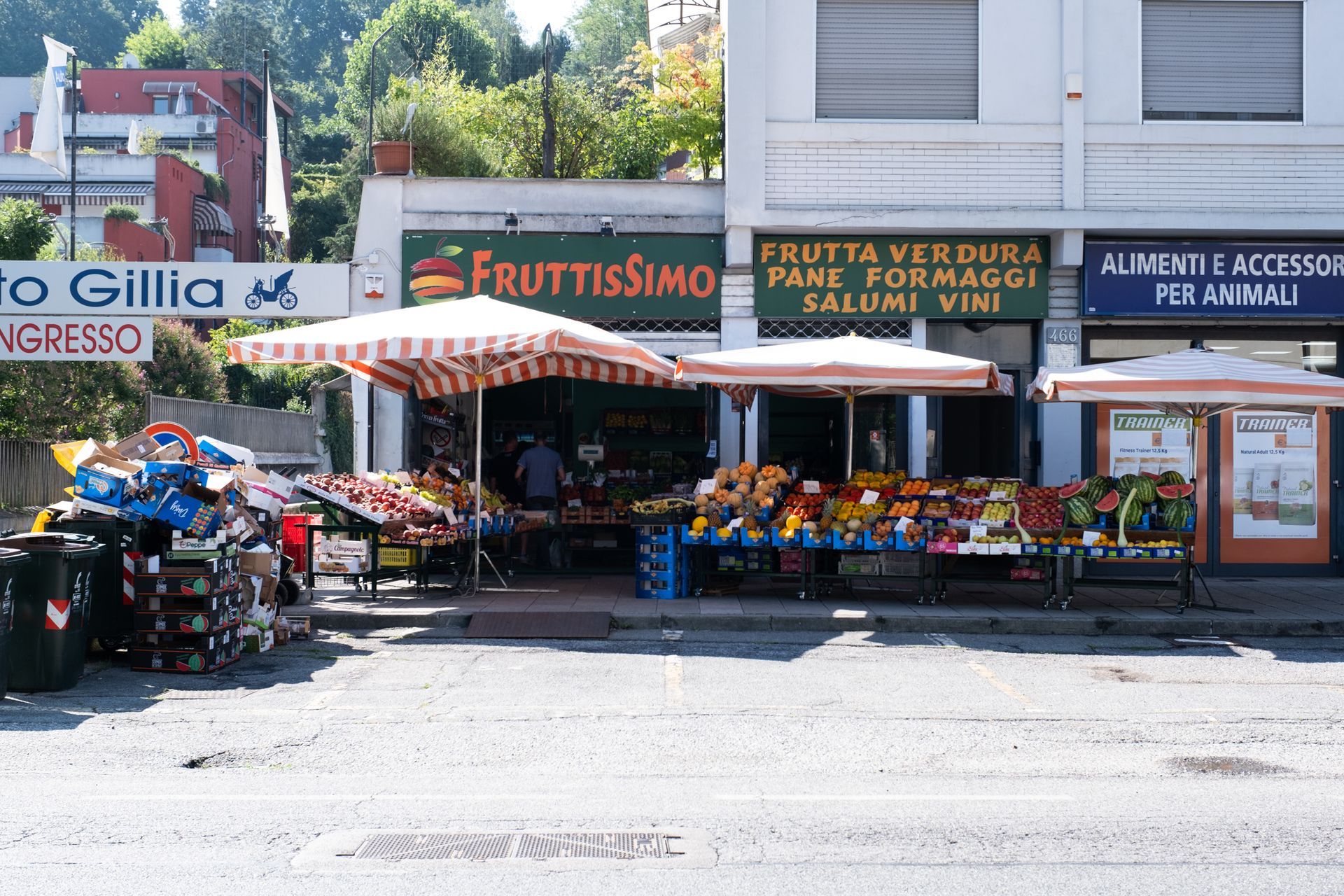 Negozio di frutta e verdura all'aperto con tenda a strisce e colorata esposizione di prodotti su una strada soleggiata