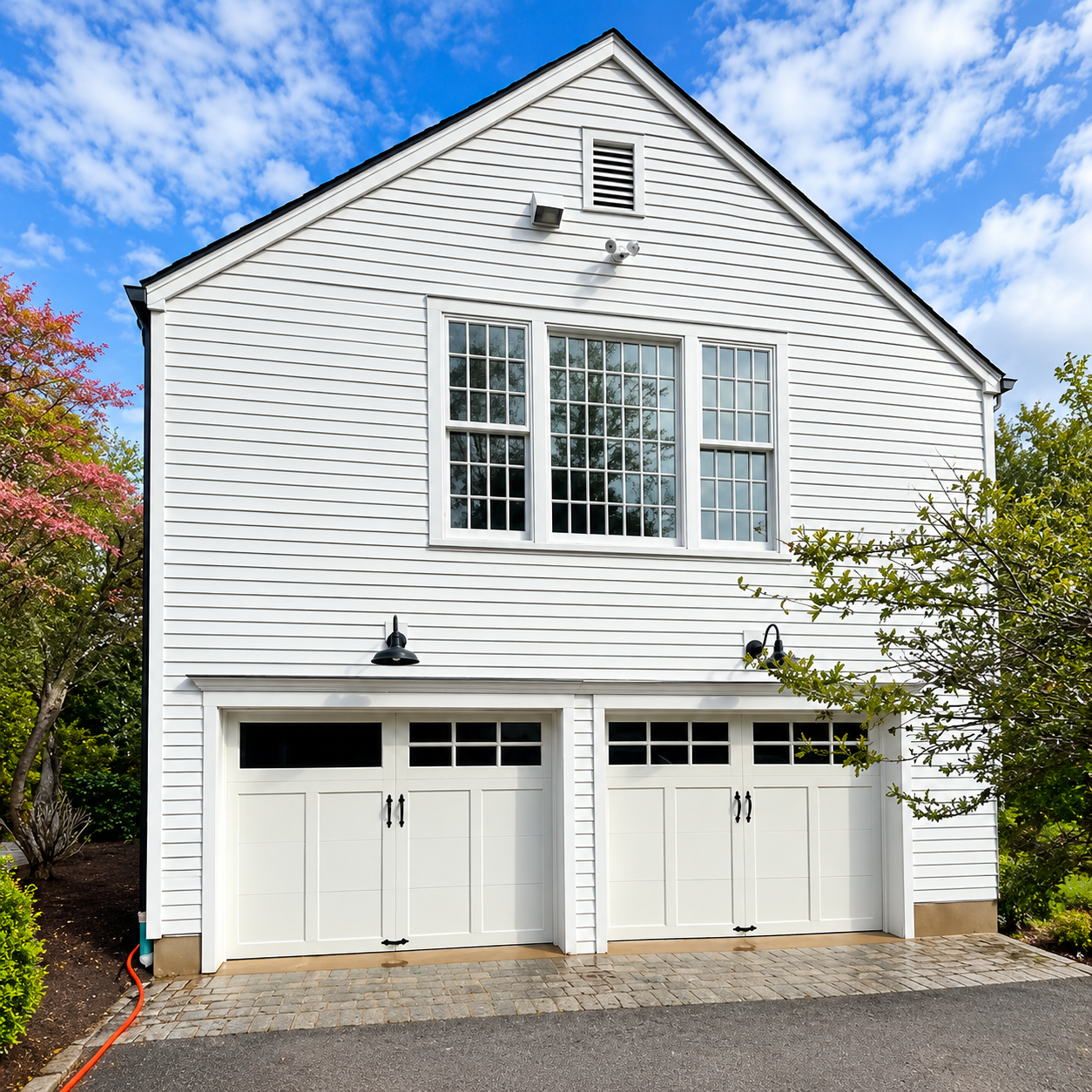 White two-story house with two garage doors, large windows, and blue sky above