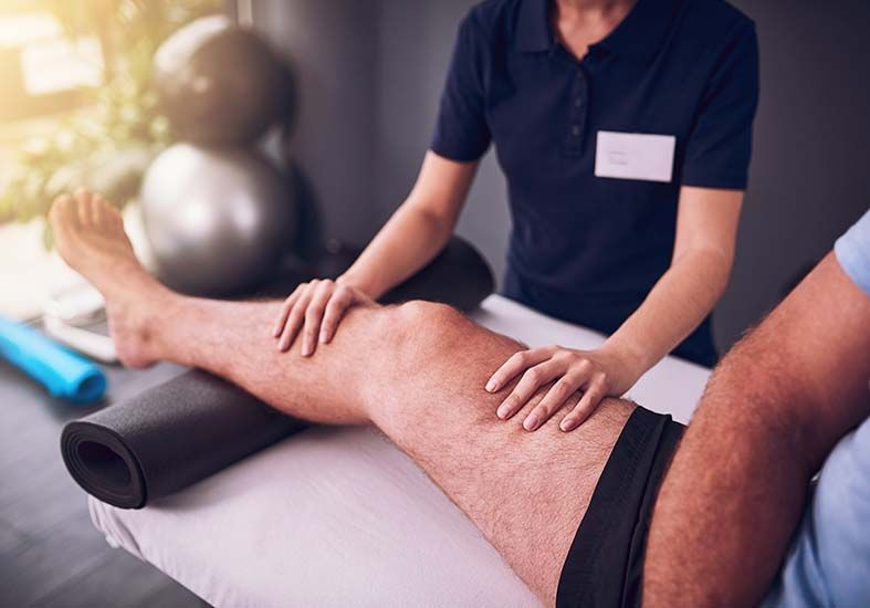 Un hombre recibe un masaje en las piernas de una fisioterapeuta.