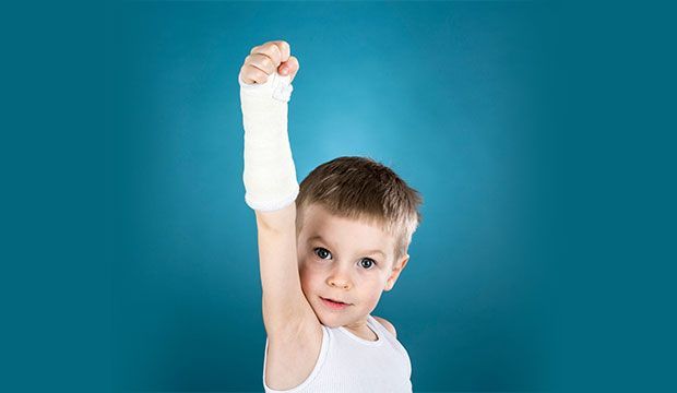 Un niño con un yeso en el brazo levanta el puño en el aire.