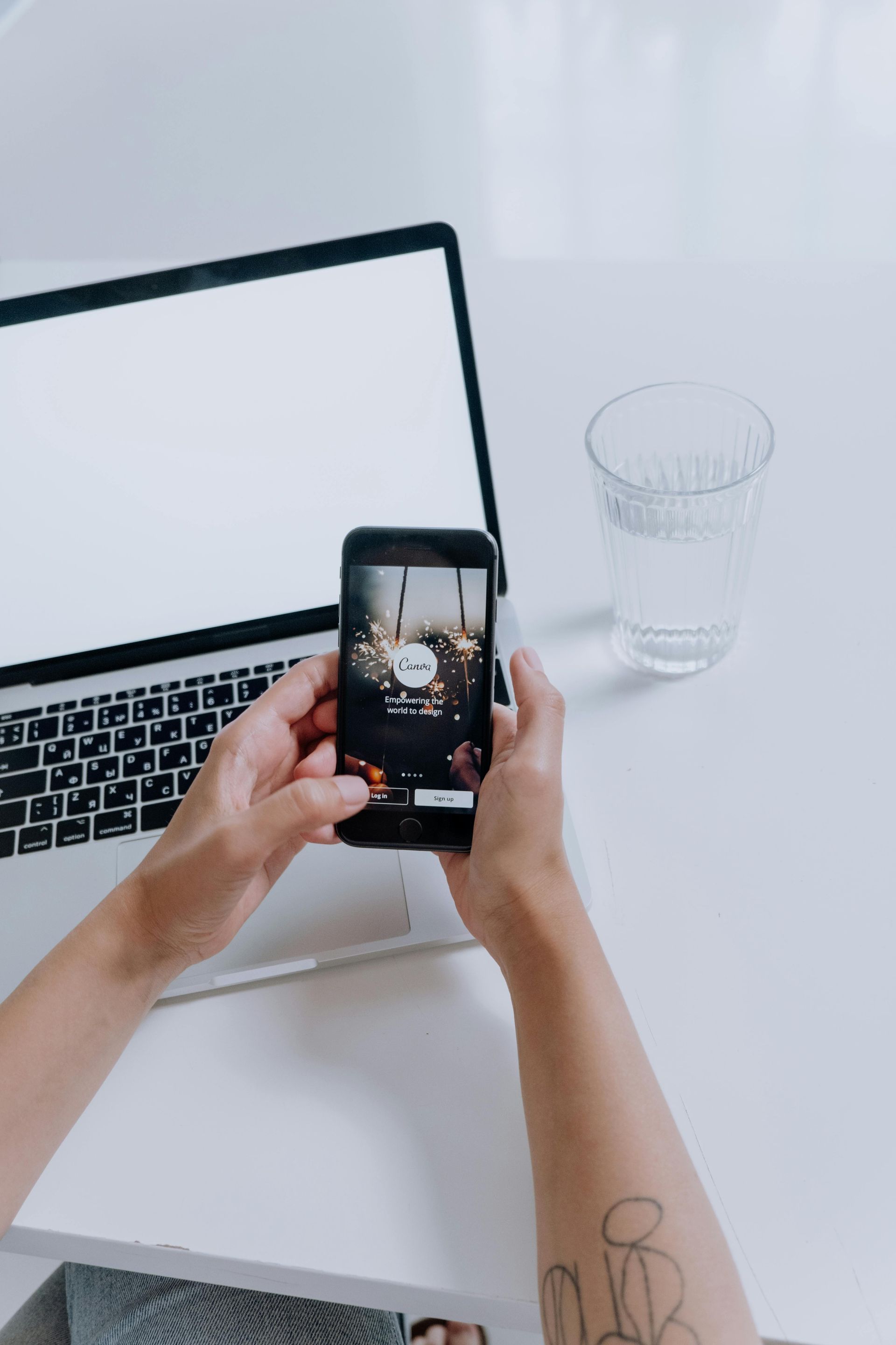 A person is holding a mobile phone in front of a laptop.