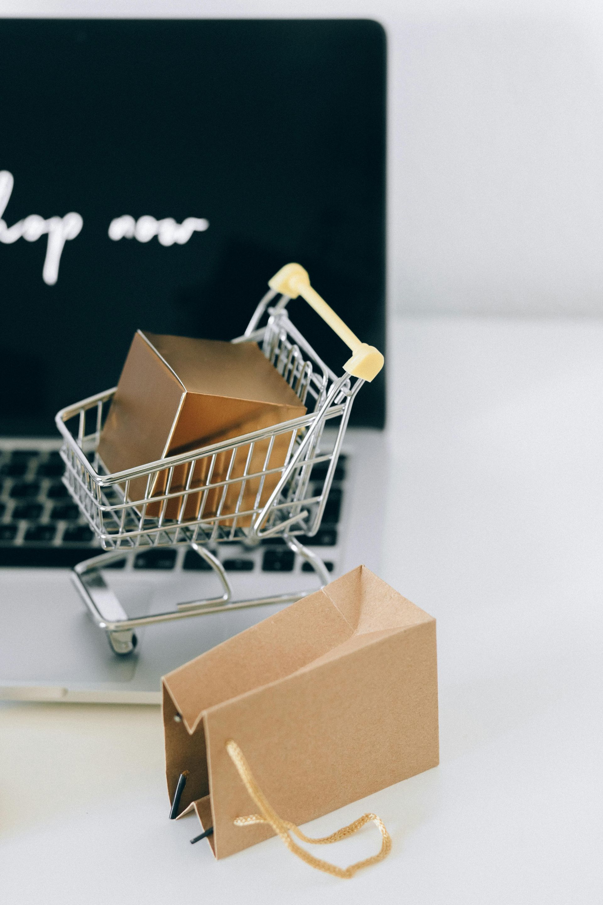 A shopping cart with boxes in it is sitting in front of a laptop.