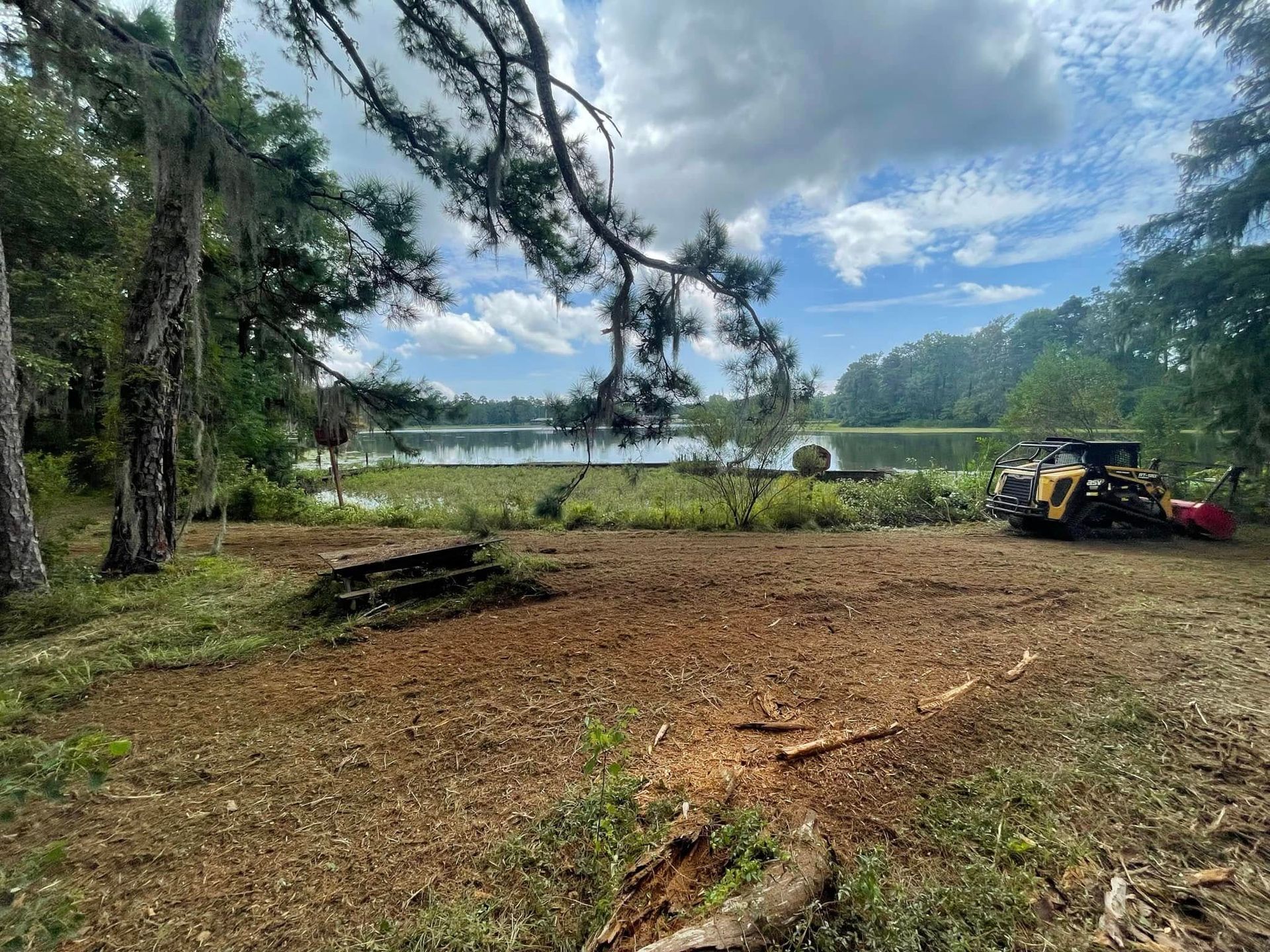 Cleared lakeside campsite with trees, cloudy sky, and a small utility vehicle on the right