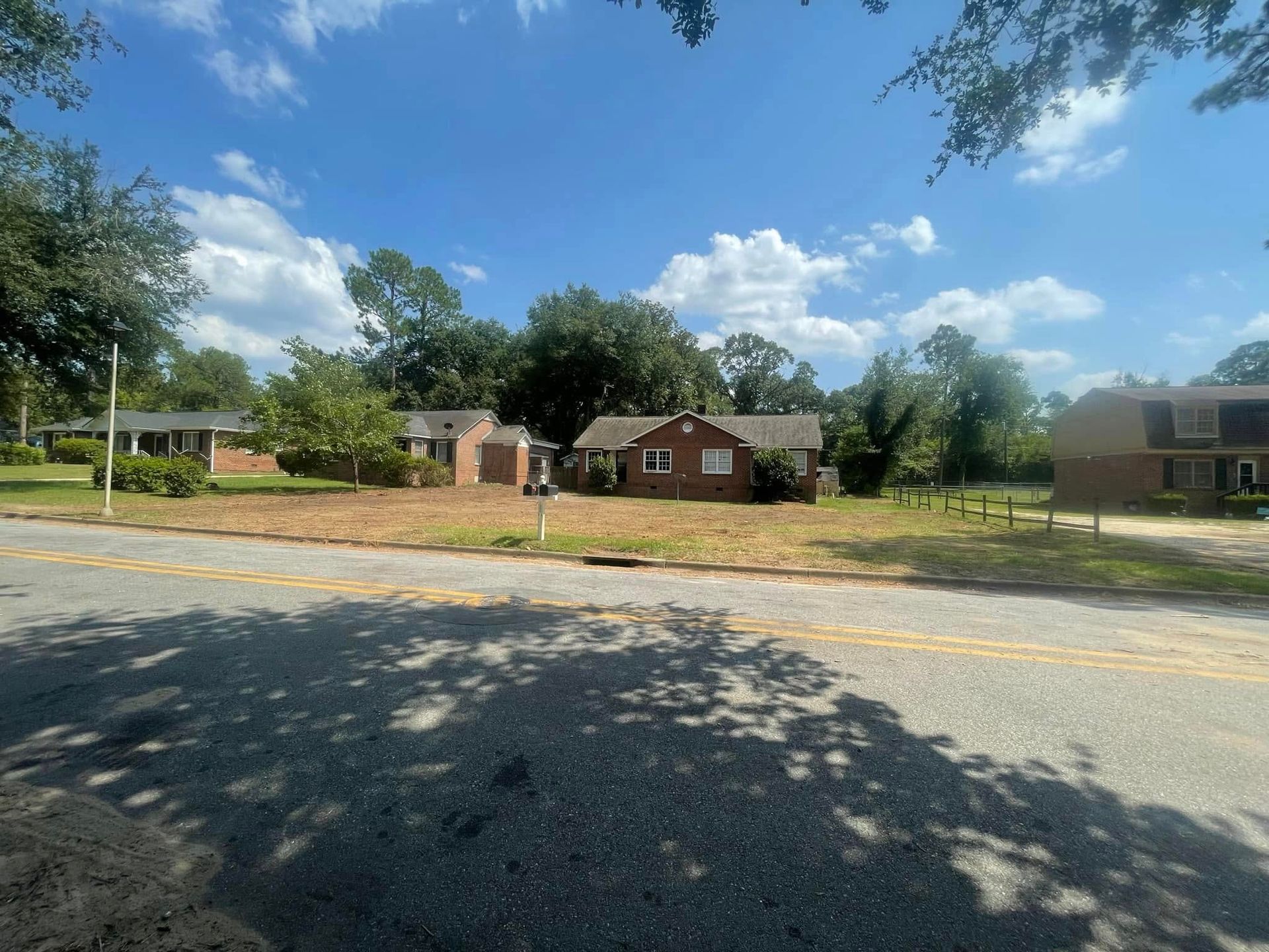Quiet suburban street with brick houses, trees, and a bright blue sky with clouds