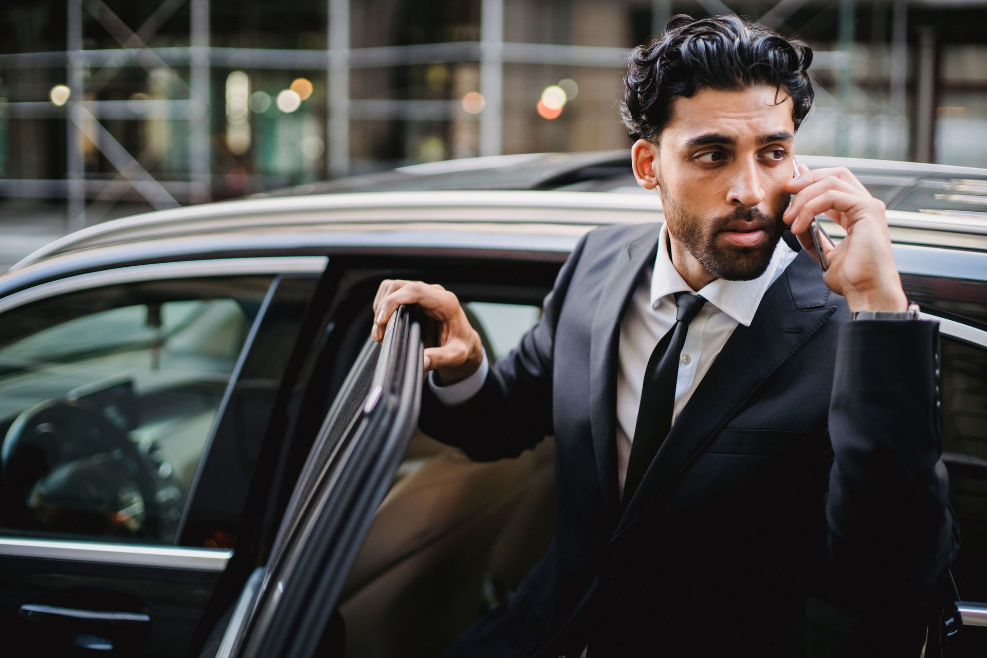 Man in a black suit stepping out of a car, adjusting his earpiece on a city street.