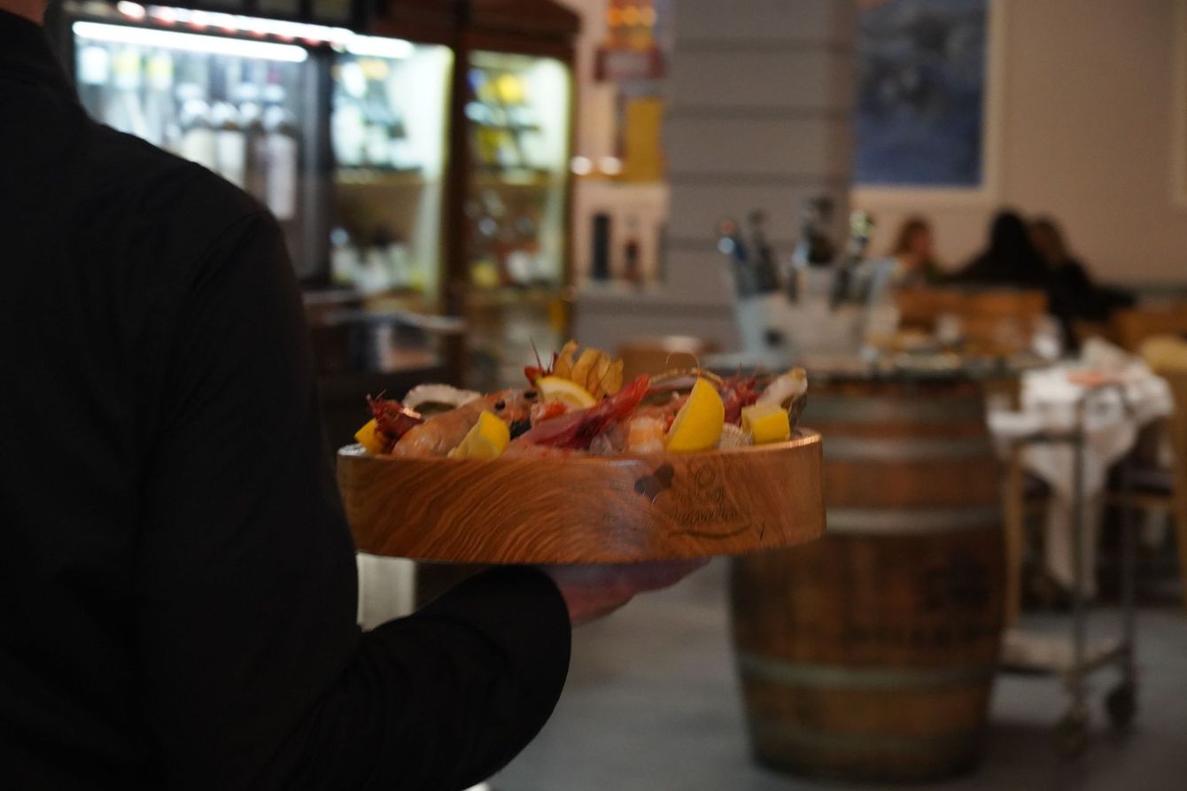 Una mano che regge un vassoio di legno con dessert colorati in un accogliente bar di ristorante.