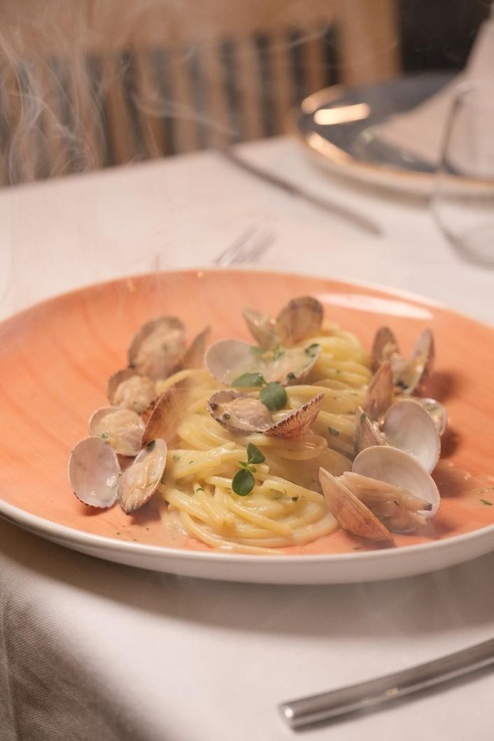 Piatto di spaghetti con vongole ed erbe aromatiche su un tavolo di ristorante.