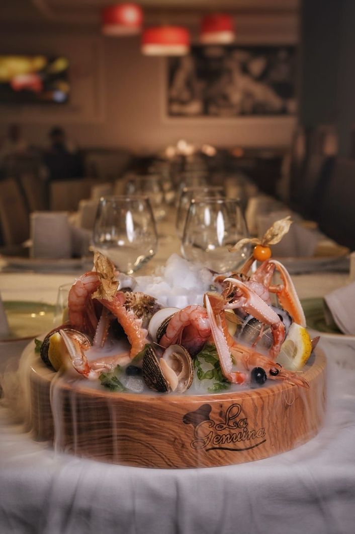 Piatto di frutti di mare con granchio, gamberi e ostriche su ghiaccio, servito al tavolo del ristorante con bicchieri da vino.