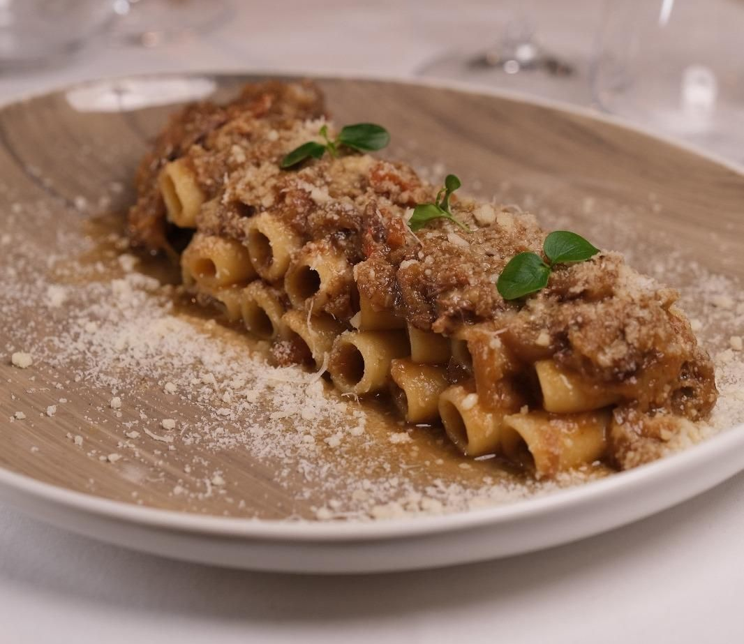 Pasta condita con ragù di carne ed erbe aromatiche su un piatto bianco, cosparsa di formaggio grattugiato.