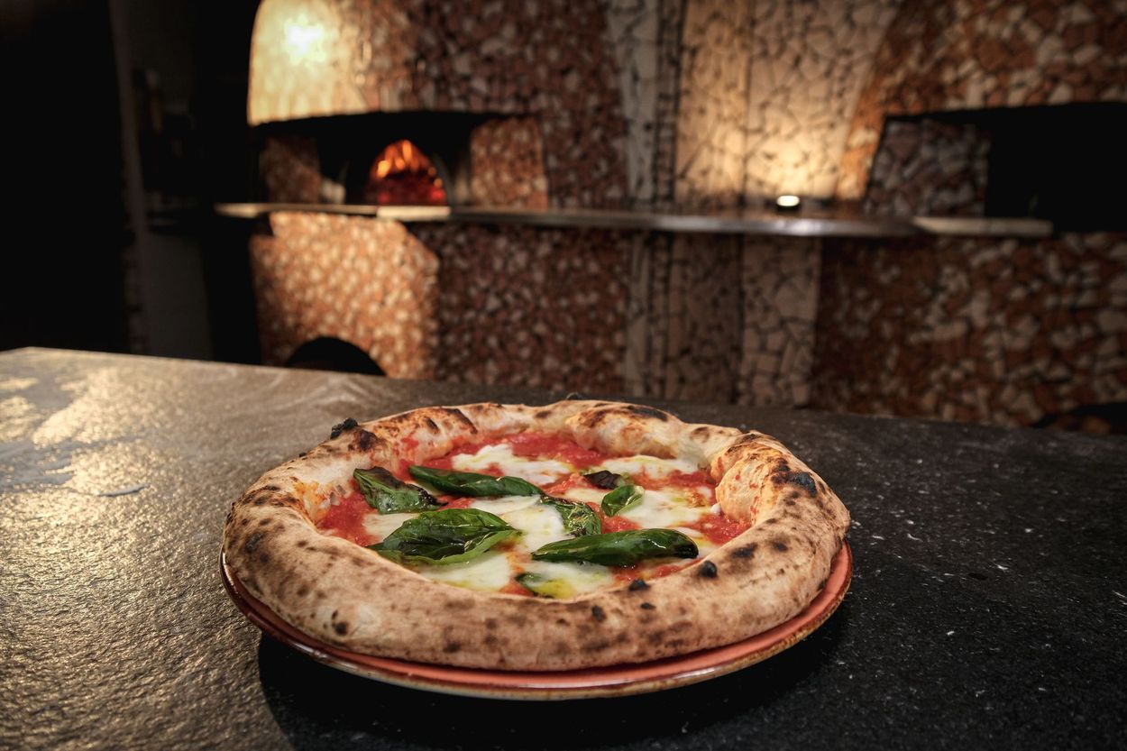Pizza con basilico e formaggio fuso su un piatto nero, su un tavolo scuro.