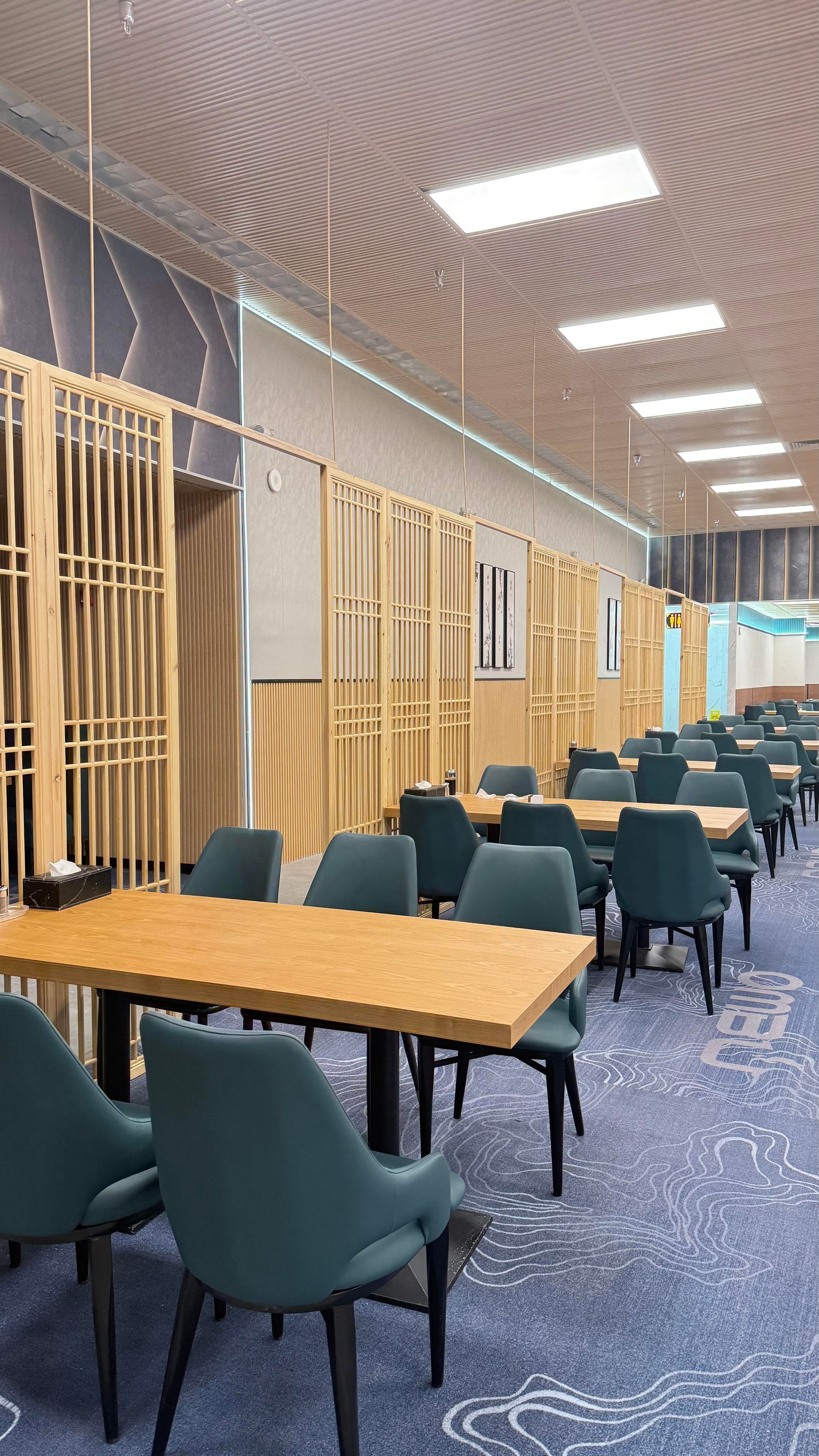 Quiet library study area with wooden tables, teal chairs, and bright ceiling lights; no people visible
