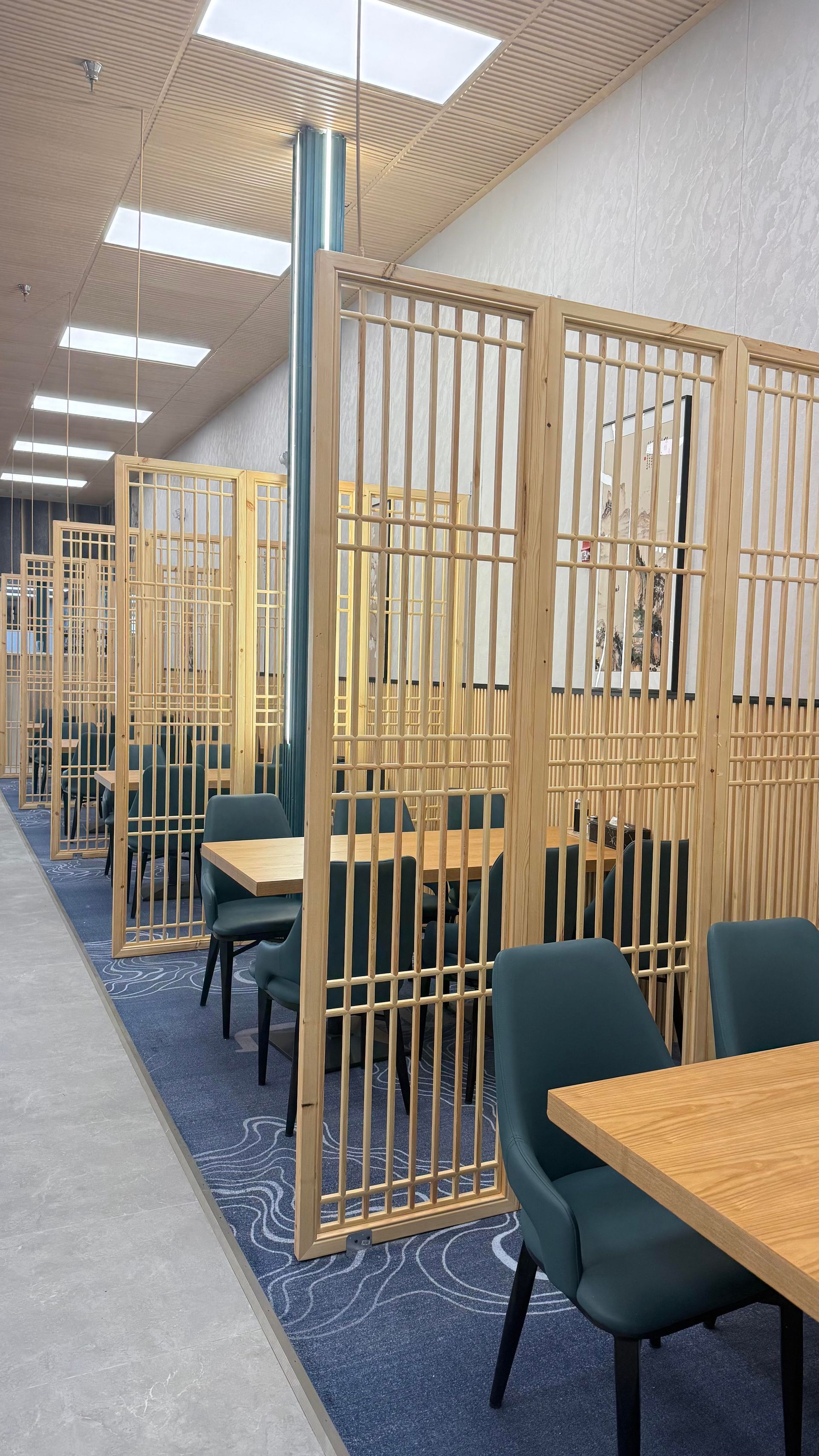 Quiet library study area with wooden privacy booths, teal chairs, and tables under bright ceiling lights.