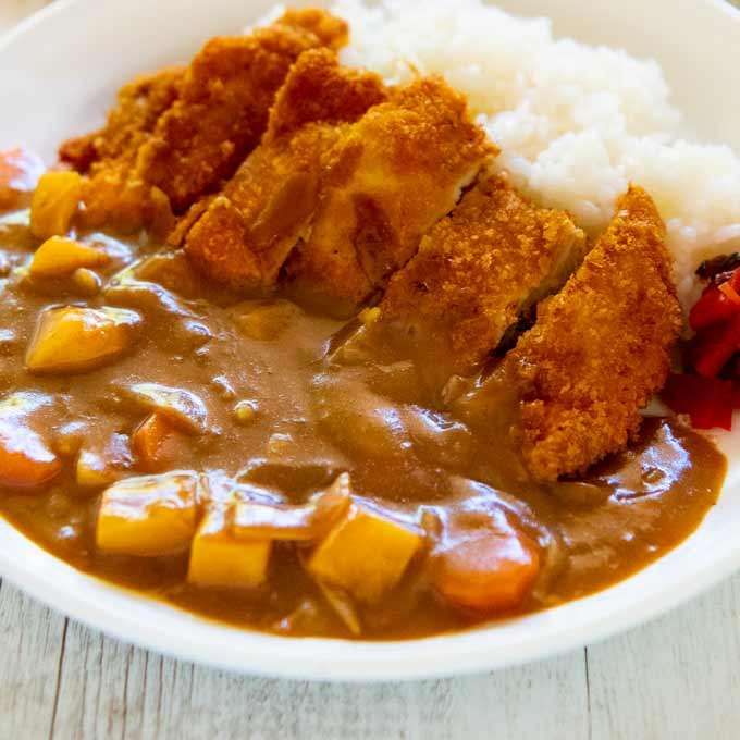 Curry rice topped with sliced breaded cutlet on a white plate