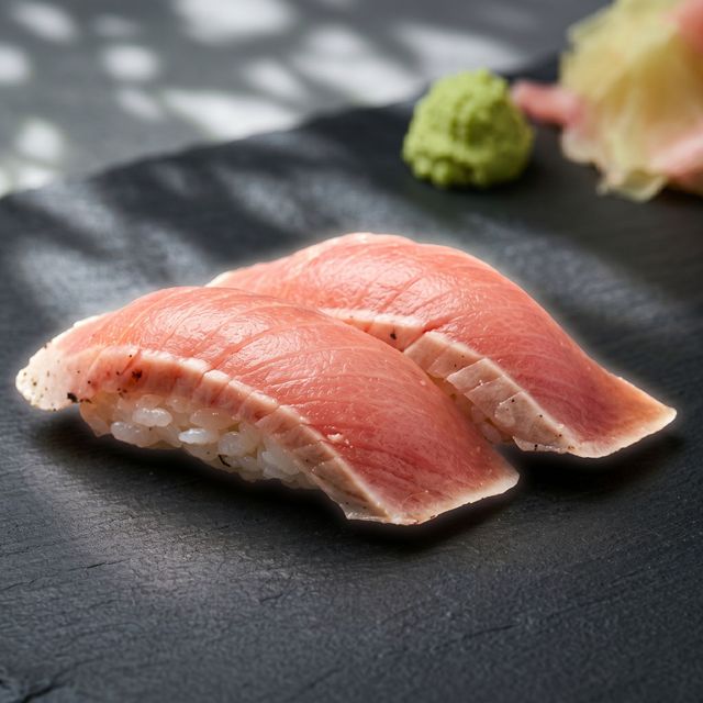 Two pieces of salmon sushi on a black plate with wasabi in the background