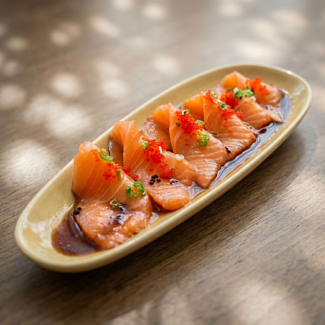 Sliced salmon sashimi on an oval plate, garnished with herbs on a wooden table.