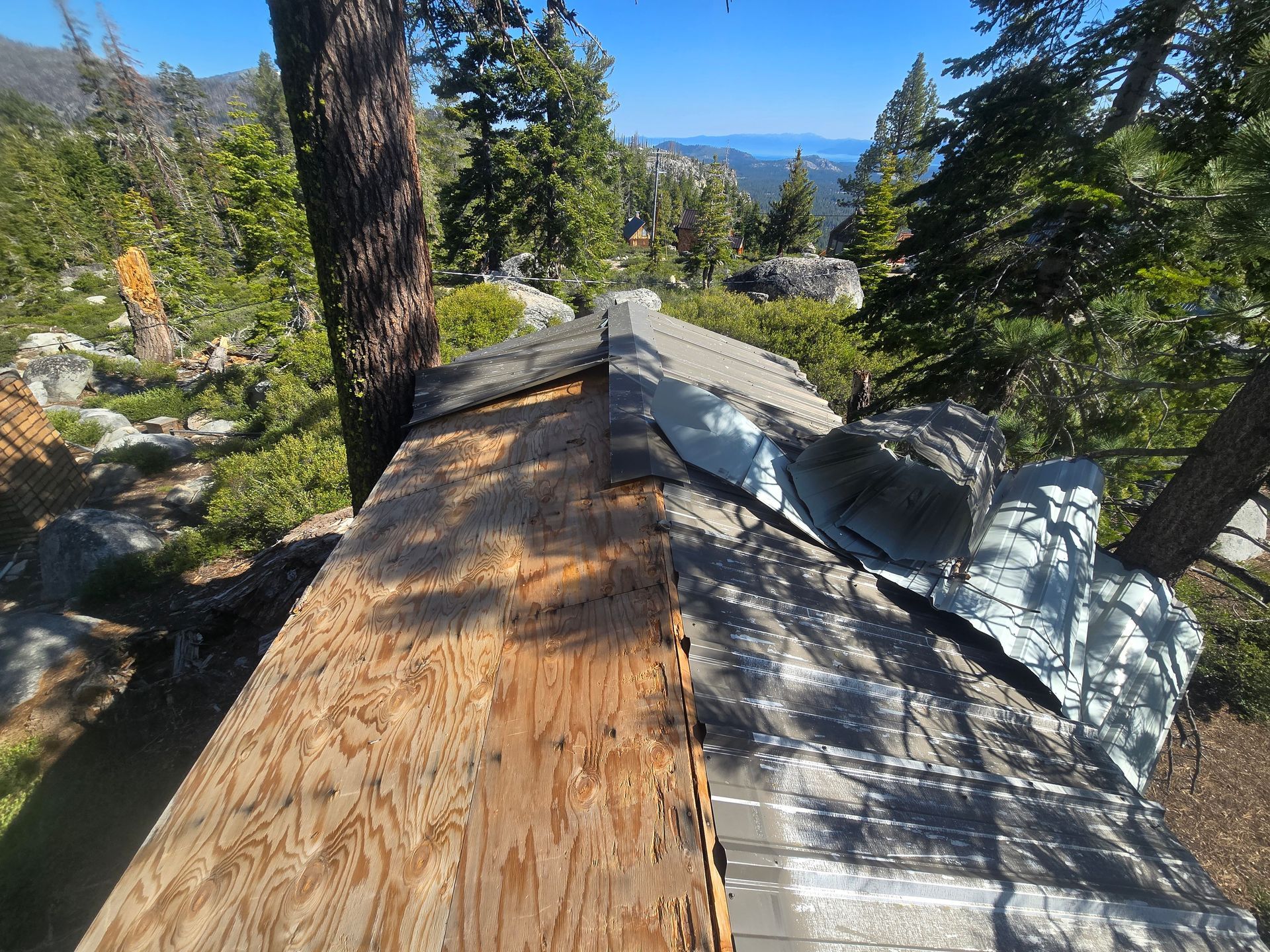 Wooden and shingled roof sections on a forested mountainside with distant blue lake and peaks view