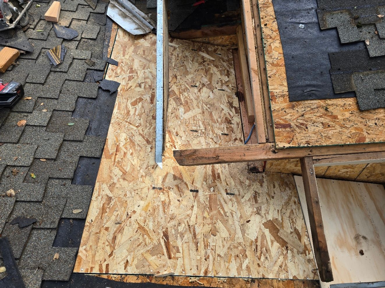 Roof under repair with exposed plywood decking and surrounding dark shingles