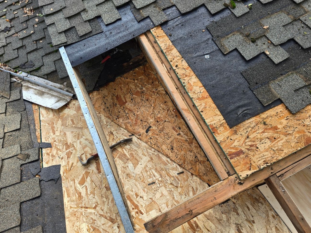 Damaged shingle roof with exposed plywood and framing around a roof opening