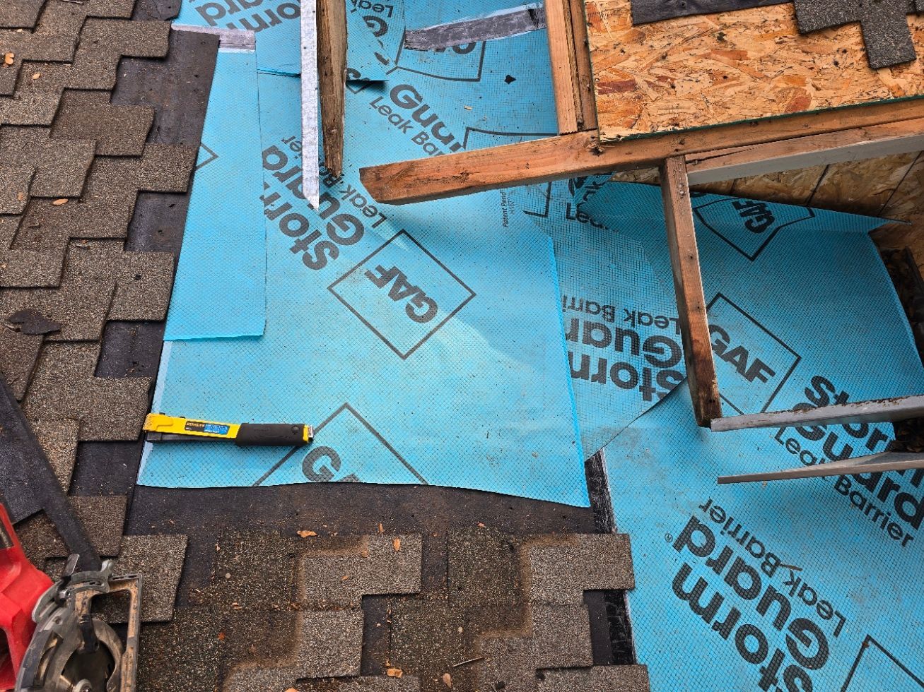 Roofing underlayment and shingles with a tape measure on a partially repaired roof.