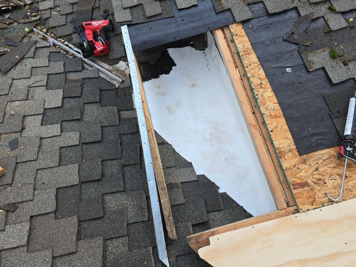 Damaged shingle roof with an open rectangular hole exposing the underlayment and plywood frame.