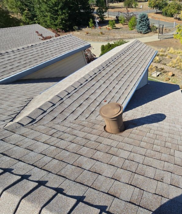 Residential roof with gray shingles and two vent pipes in daylight