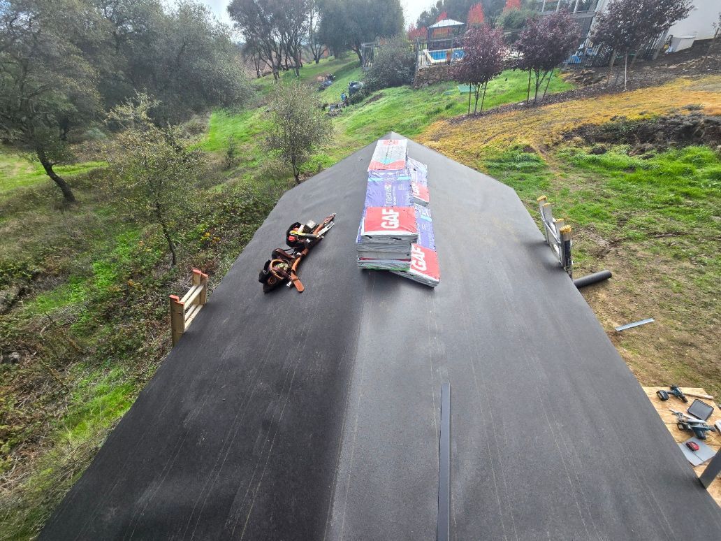 Black road surface with construction materials laid out in a grassy outdoor area