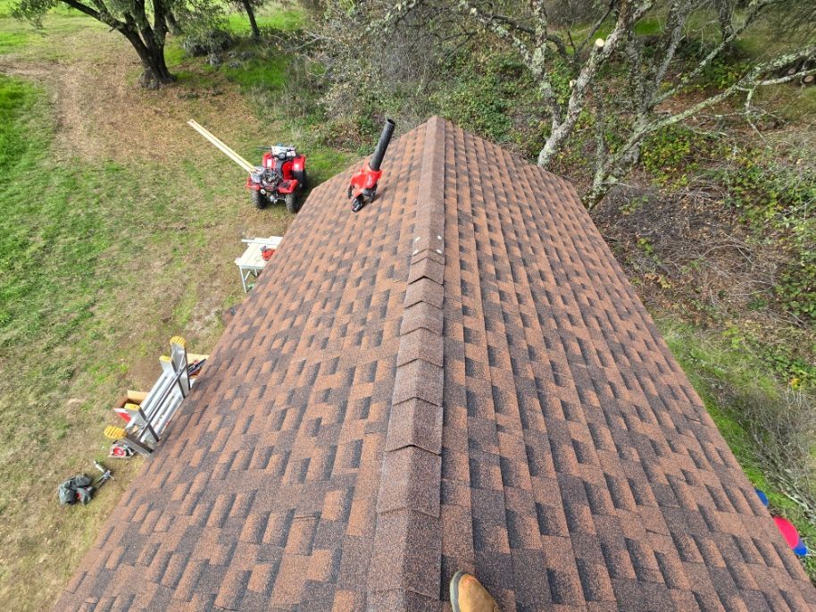 Roofing workers on a shingled roof, with tools and equipment along the eaves below.
