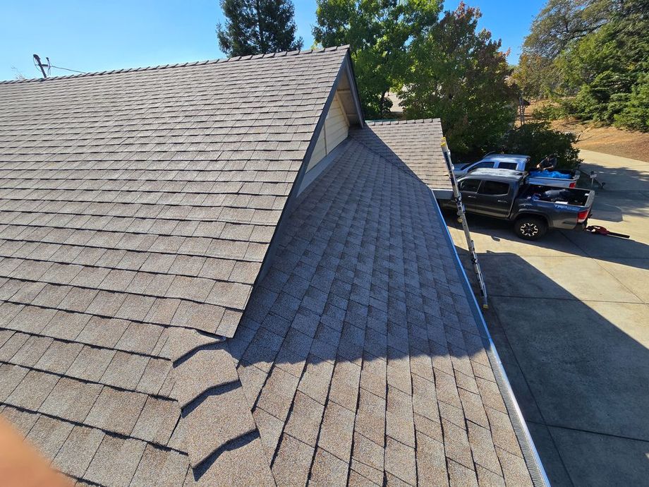Roof shingles on a house with a valley seam, driveway, and parked black pickup under a sunny sky