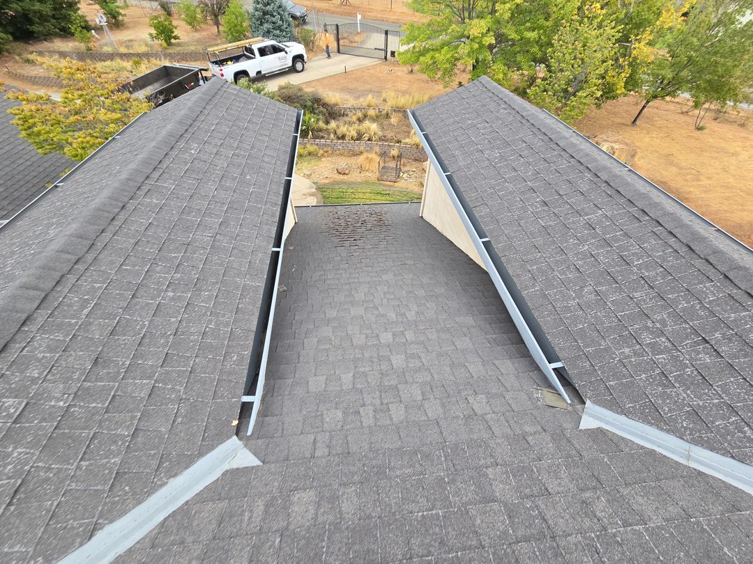Rooftop view between two shingled slopes, overlooking a yard and a white vehicle below.