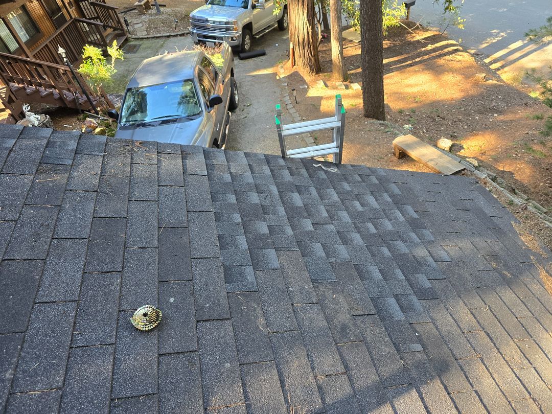 Snow-dusted roof overlooking a driveway with parked cars and a wooded yard below