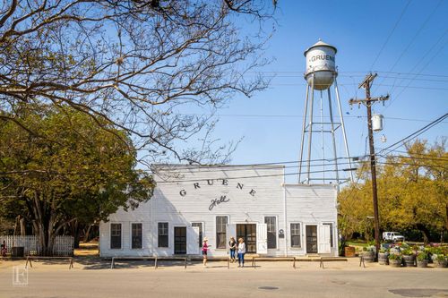 White historic building with a tall water tower under a clear sky, with people outside and trees nearby