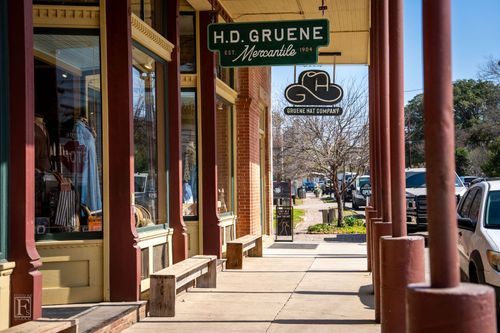 Historic downtown sidewalk with storefronts and hanging signs on a sunny day