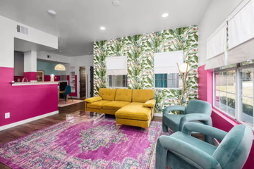 Bright living room with yellow sofa, teal chairs, pink rug, and tropical leaf accent wall