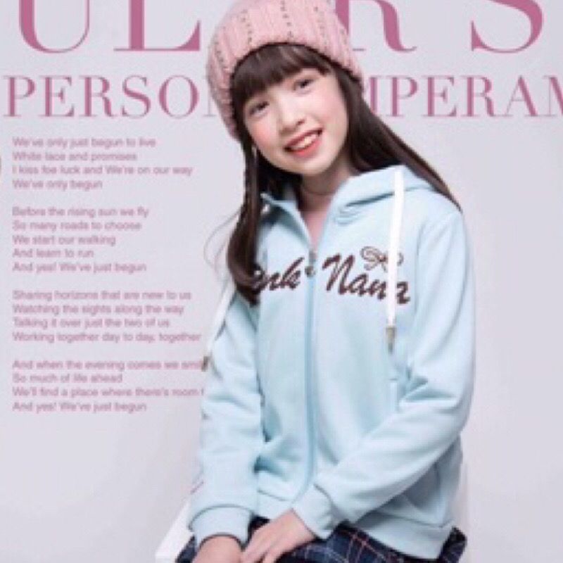 戴著粉紅色無帽沿帽和藍色連帽衫的小女孩微笑著。文字部分可見。