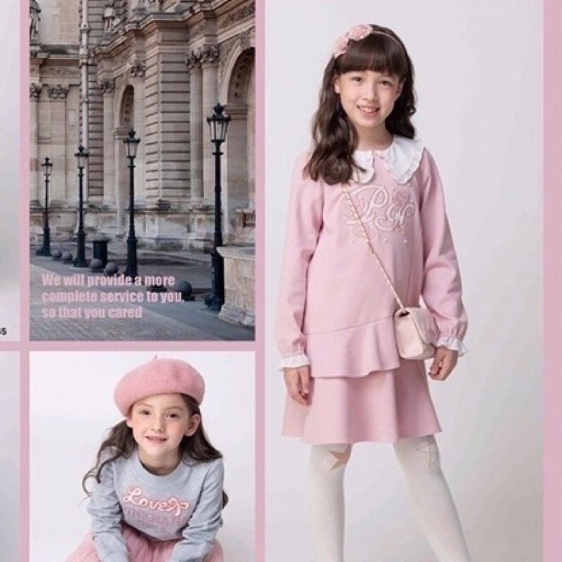 一位身穿粉紅色洋裝、頭戴髮帶的女孩微笑著擺姿勢拍照。白色緊身褲和手提包讓她的造型更加完美。