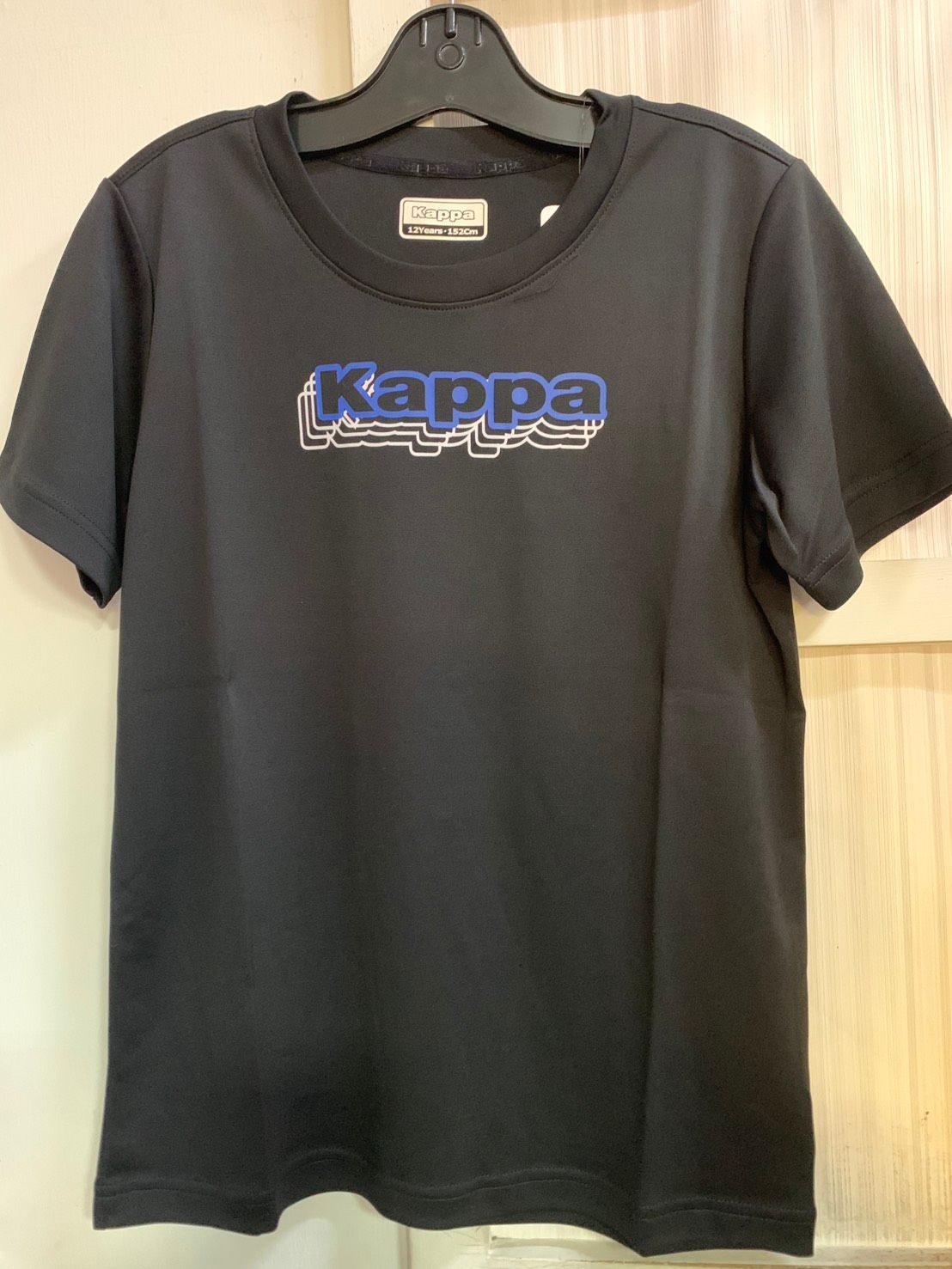 黃色的 Kappa T 卹，帶有黑色和黃色的標誌，掛在黑色的衣架上。