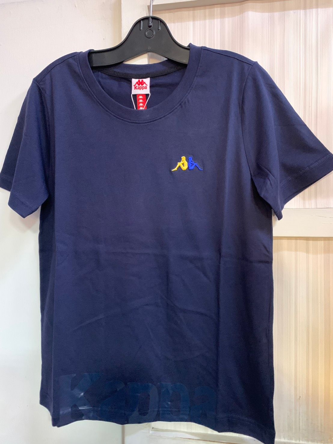 胸前有小標誌的海軍藍色 Kappa T 卹，掛在黑色衣架上。