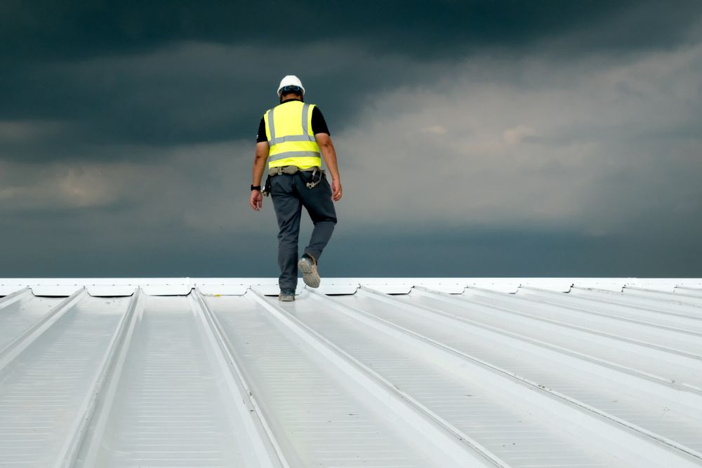 A Man Is Walking On Top Of A White Roof — Roof & Guttering Solutions In Woy Woy, NSW