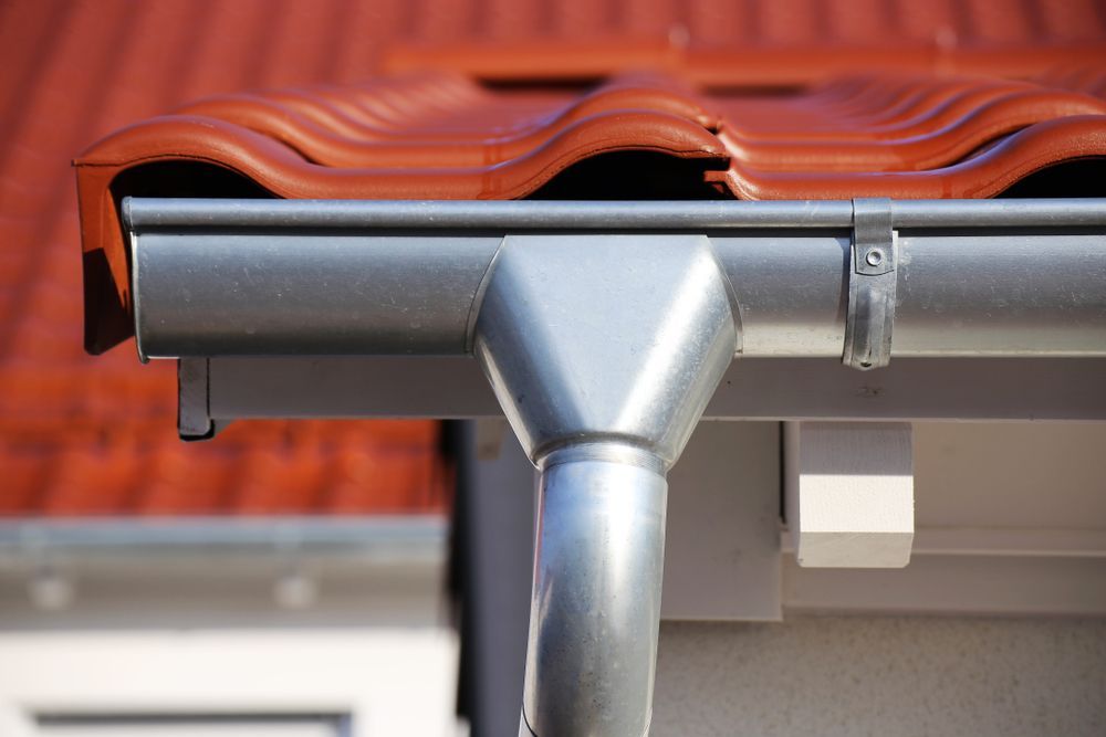 A Close Up Of A Gutter On A Roof With A Red Tile Roof — Roof & Guttering Solutions In Gosford, NSW