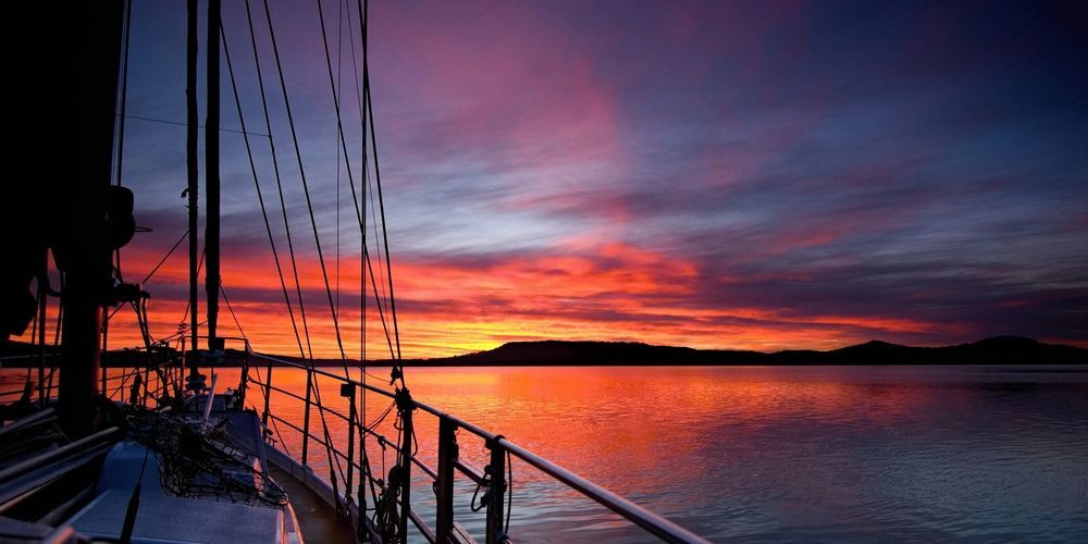 A Sailboat Is Floating On Top Of A Body Of Water At Sunset — Roof & Guttering Solutions In Gosford, NSW